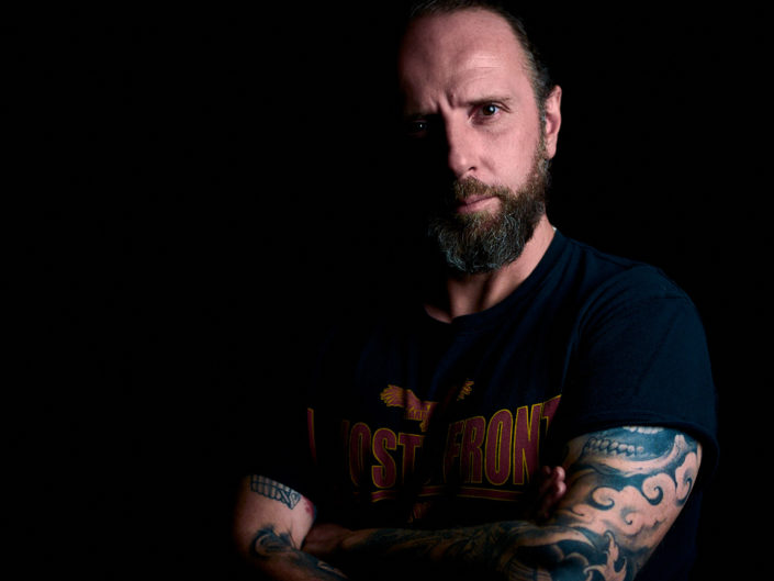 Portrait studio sur fond noir d'un homme avec une barbe et des tatouages, type personal branding